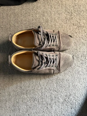 Loubs väll andvänds men äkta  - Grå sneakers i mocka med klassisk snörning och låg profil. Skorna har en enkel design med rund tå och diskreta sömmar. Insidan är ljusbeige och sulan är platt. Perfekta för en avslappnad stil.