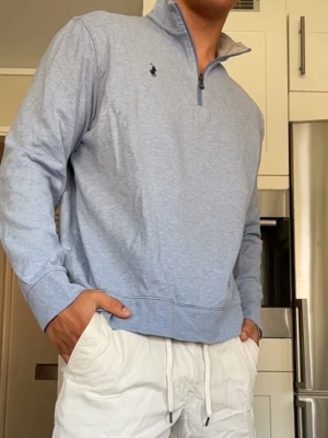 Ljusblå quarter zip från Ralph Lauren - Ljusblå långärmad tröja med quarter zip och liten broderad logga på bröstet. Tröjan har en avslappnad passform och är tillverkad i mjukt material, perfekt för en chill och stilren look.