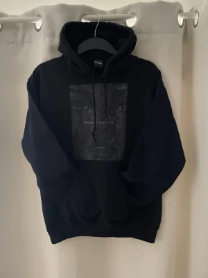 Snygg hoodie med tryck  - Tjo! Säljer en svart hoodie med huva och snören. På bröstet finns ett tryck med texten 'Positivité est priorité' och ett konstnärligt motiv i gråskala. Hoodien har en klassisk känguruficka och ribbade muddar. Perfekt för en grisch och laidback stil. Skicket är 9,5/10 och storleken är S passar 174-180 ungefär!! Hör av dig vid mer frågor eller funderingar🕺mvh Ga😁🤩