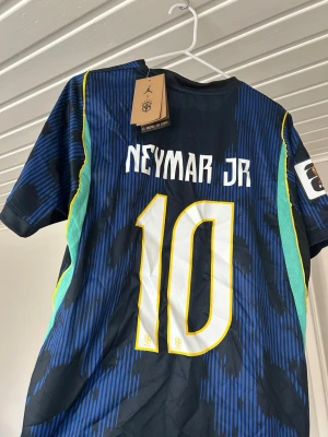 Brasilien Neymar Jr matchtröja blå - Säljer en blå Brasilien matchtröja med Neymar Jr och nummer 10 på ryggen. Tröjan har gula och gröna detaljer, CBF-logga och Jordan-logga på bröstet. Tillverkad i lätt och ventilerande material, perfekt för fotboll eller träning.