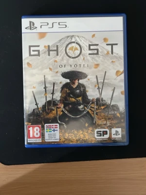 Ghost of Yotei PS5 spel - Ghost of Yotei till PS5 är ett actionäventyrsspel med japanskt tema. Omslaget visar en samuraj med flera svärd framför ett berg och fallande löv. Spelet har en blå plastfodral och är PEGI 18-märkt. Perfekt för dig som gillar episka berättelser och snygg grafik.