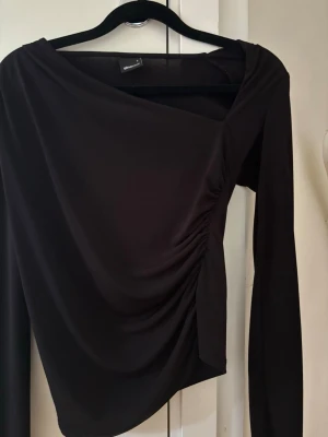 Svart asymmetrisk topp   - Snygg svart topp med draperad detalj på sidan i storlek S från Gina 