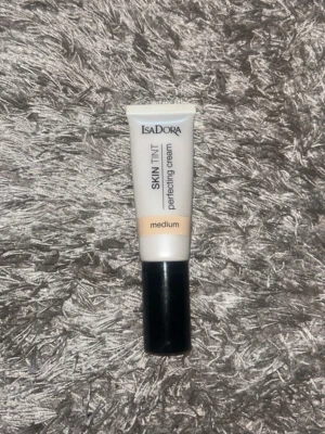 IsaDora Skin Tint Perfecting Cream - IsaDora Skin Tint Perfecting Cream i nyansen medium. Tuben är vit med svart kork och har en beige färgremsa som visar nyansen. Perfekt för en naturlig och jämn bas. Enkel att applicera och smälter fint in i huden.