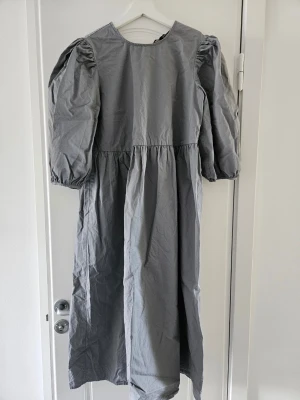 Grå långklänning från Selected Femme stl 36 - Säljer en stilren grå långklänning från Selected Femme med puffärmar och rund halsringning. Klänningen har en rak passform och är tillverkad i ett mjukt tyg som känns skönt mot huden. Perfekt för dig som gillar minimalistisk och trendig stil.