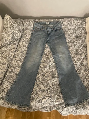 Ljusblå bootcut jeans med brodyr - Säljer ett par ljusblå bootcut jeans med snygg slitning framtill och broderade detaljer på. Perfekta för dig som vill ha ett par jeans med unik touch!