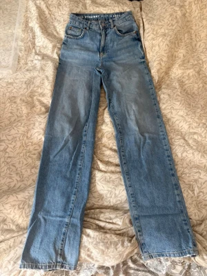 Ljusblå raka jeans med hög midja - Säljer ett par ljusblå jeans med rak passform och hög midja. Klassisk femficksmodell och dragkedja med knapp. Jeansen har en avslappnad look och är perfekta för en trendig vardagsstil.