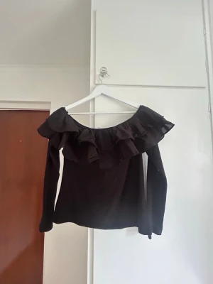 Svart topp med volang och offshoulder - Snygg svart topp med bred volang runt axlarna och offshoulder!