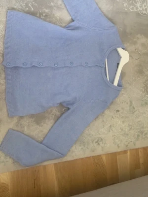 Ljusblå kofta med knappar - Supersöt ljusblå kofta med rund hals och matchande knappar framtill. Koftan har långa ärmar och ribbade muddar vid ärmslut och nederkant. Perfekt att slänga över en topp för en chill look.