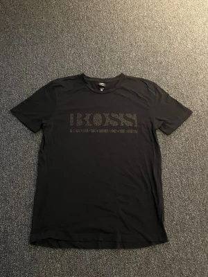 Svart t-shirt från BOSS - Snygg svart t-shirt från BOSS med diskret logga framtill. Klassisk rund halsringning och korta ärmar. Perfekt till jeans eller shorts för en clean och stilren look.