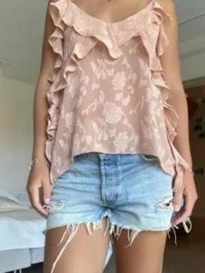 Rosa blommig blus med volanger från Zara  - Säljer en beige linnetopp med tunna axelband och volangdetaljer längs kanterna. Toppen har ett subtilt blommigt mönster och en v-ringad halsringning. Perfekt för dig som gillar en romantisk och luftig stil. Blusen är från Zara och har används vid 1 tillfällle. Inget att anmärka på priset går att diskutera. Första bilden är lånad för att visa hur den sitter på ❤️