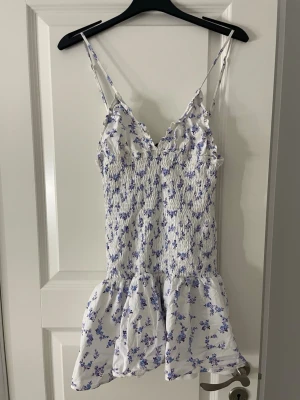 Blommig Zara klänning  - Söt vit kortklänning med blått och lila blommönster. Klänningen har smala axelband, smockad överdel och volang nedtill. Pris kan diskuteras. Aldrig använd endast testad!💗