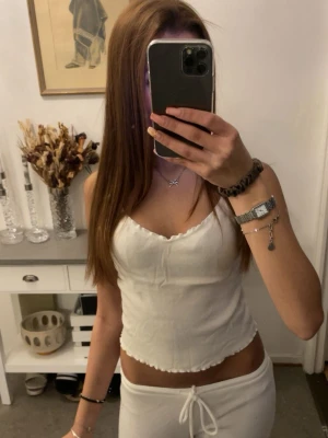 Vit ärmlös linnetopp med volangkant - Säljer en söt vit linnetopp med volangkant och v-ringning. Toppen är ärmlös och har en croppad passform som ger en trendig look. Perfekt att matcha med jeans eller kjol för en stilren outfit.