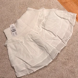 Vit kortkjol med volang från Gina Tricot - Supersöt vit kortkjol från Gina Tricot Young med volangdetaljer. Kjolen är gjord i ett lätt och luftigt material, perfekt för varma dagar. Stl. 146/152