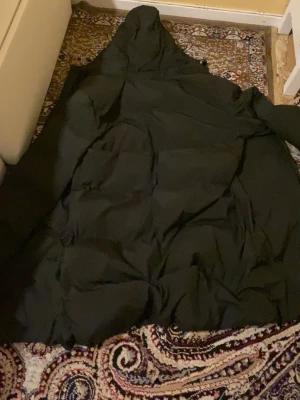 Svart lång dunjacka med huva - Säljer en svart lång dunjacka med huva. Jackan har en puffig design och är perfekt för kalla vinterdagar. Tillverkad i Kina och har en klassisk look som funkar till det mesta. Materialet är typiskt för dunjackor och ger bra värme.