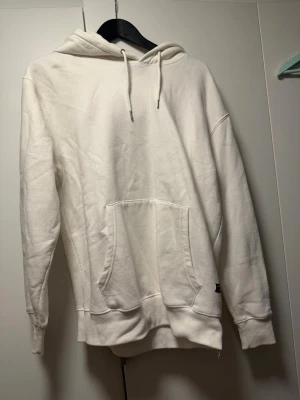 Vit hoodie från Jack & Jones - Snygg vit hoodie från Jack & Jones med klassisk känguruficka och dragsko i huvan. Tillverkad i mjukt material som känns skönt mot huden. Perfekt för en avslappnad och stilren look.