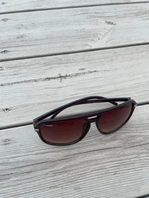  solglasögon från Vestimo - Snygga solglasögon från Vestimo med svart båge och mörkröda tonade glas. Klassisk pilotform med metall-detalj vid näsryggen. Perfekta för soliga dagar och ger en cool vibe till din outfit.