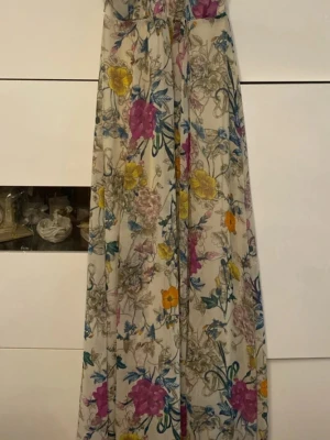 Blommig långklänning med halterneck - Säljer en romantisk långklänning med halterneck och färgglatt blommönster i rosa, gul, blå och orange på ljus botten. Klänningen har en luftig passform och tunna axelband som knyts i nacken. Perfekt för sommarens alla tillfällen!