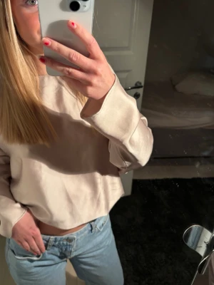 Beige croppad blus med långa ärmar - Trendig beige croppad blus med avslappnad passform och långa ärmar. Perfekt att matcha med jeans för en chill look. jätte söt och även lite cool  och champagnefärgad blus