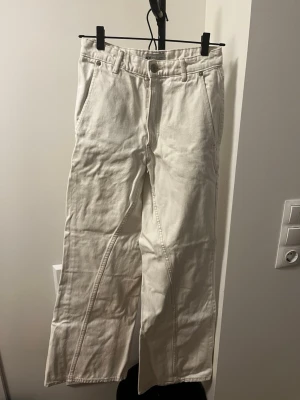 Vida vita jeans med raka ben - Säljer ett par snygga vita Zara jeans med vida, raka ben och hög midja. Jeansen har klassiska fickor fram och bak samt bälteshällor. Perfekta för en clean och trendig look. Materialet är kraftig denim i bomull. Lite fläckiga efter användning samt lagad vid höger bakficka.