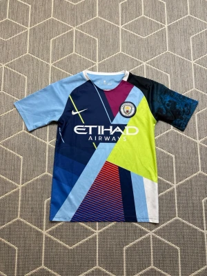 Manchester City Nike  - Säljer en färgstark Manchester City matchtröja från Nike med grafiskt mönster i blått, ljusblått, limegrönt, vinrött och svart. Tröjan har klubbmärke på bröstet och Etihad Airways-logga framtill. Tillverkad i lätt och ventilerande polyester, perfekt för fotbollsträning.