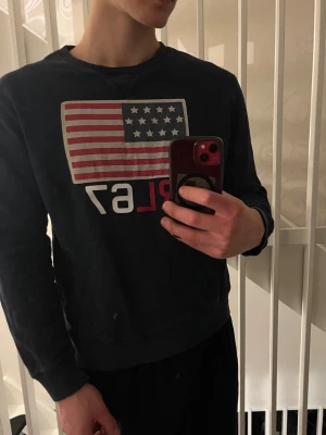 Polo Ralph Lauren tröja - Mörkblå sweatshirt från Polo Ralph Lauren med amerikansk flagga och RL67 tryck på bröstet. Flaggan är gjort av tyg och siffrorna är tryckta. Perfekt för en avslappnad och stilren look. Storlek XL med passar M‼️Pris kan diskuteras💰