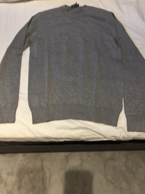 Grå slim fit tröja från H&M - Snygg grå tröja från H&M i slim fit-modell. Tröjan har rund halsringning, långa ärmar och ribbade muddar vid ärmslut och nederkant. Perfekt för lager på lager och enkel att matcha med olika outfits.