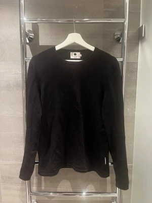 Svart stickad tröja från N.N.0.7 - Klassisk svart stickad tröja från N.N.0.7 med rund halsringning och långa ärmar. Enkel och stilren design som passar perfekt till lager-på-lager. Tillverkad i mjukt material för en bekväm känsla. Nypris ca: 1000kr. Storlek S (står L men råkade tvätta fel). Skriv vid frågor!
