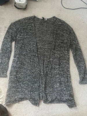 Svartvit lång kofta från H&M - Mysig lång kofta från H&M i svartvitt melerat garn. Koftan har öppen front utan knappar, långa ärmar och en avslappnad passform. Perfekt att slänga över en t-shirt eller topp för en chill look.