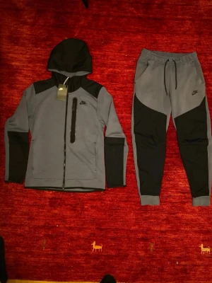 Nike Tech Fleece tracksuit - Nike Tech Fleece tracksuit- Super snygg tvådelad set i grått och svart. Består av hoodie med dragkedja och matchande byxor. Perfekt passform, varm och lätt - klassisk Nike - kvalitet 