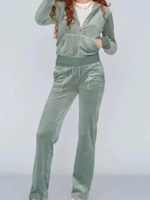 Grå velourset från Juicy Couture - Mjuk och lyxig grå velourset från Juicy Couture med dragkedja på luvtröjan och breda muddar. Byxorna har raka ben och resår i midjan samt fickor fram. Perfekt för chill dagar hemma eller när du vill vara extra bekväm.