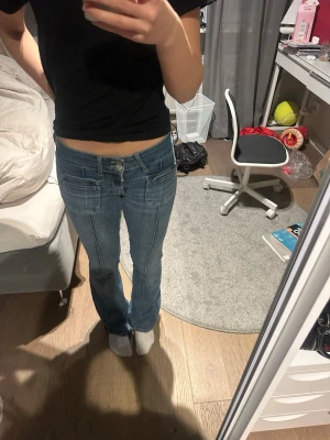 Blå bootcut jeans med fickor - Säljer ett par blå bootcut jeans med fram- och bakfickor samt markerade sömmar framtill. Jeansen har låg midja och klassisk denimlook. Perfekta för dig som gillar en avslappnad men trendig stil. Materialet är mjuk denim i bomull.