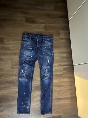 Mörkblå distressed jeans med färgstänk - Snygga mörkblå jeans med slitningar, färgstänk och råa benslut. Jeansen har fem fickor och en smal passform som ger en trendig look. Perfekta för dig som gillar en edgy streetstil. Materialet är klassisk denim i bomull.