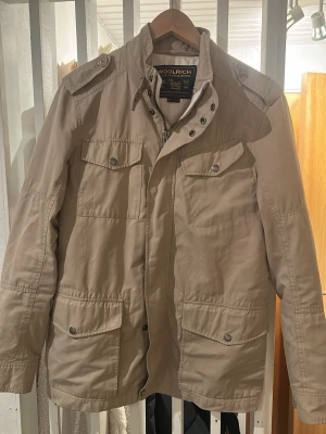 Beige Fieldjacket från Woolrich - Fieldjacket från Woolrich i nyskick. Populär modell. Storlek Medium. Pris 899. Skriv vid funderingar!🙌
