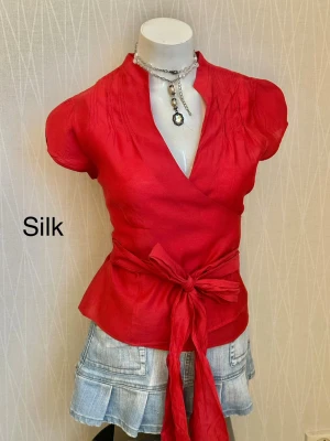 Röd omlottblus i siden - Snygg röd omlottblus i 21% siden med knytband i midjan och korta ärmar. M/L