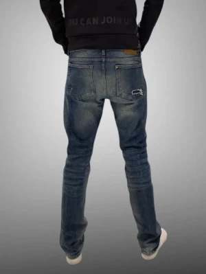 Blå slitna jeans med hål - Säljer ett par blå jeans med slitningar och hål på både fram- och baksida. Jeansen har klassisk femficksmodell, normal midja och raka ben. Materialet är denim i bomull och de har en avslappnad streetstil.