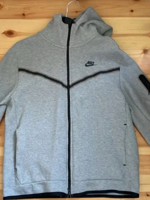 Grå Nike hoodie med dragkedja - Snygg grå Nike Tech Hoodie med dragkedja. Mjukt material och är använd endast 2-3 gånger. 