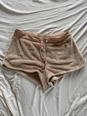Beiga mjukisshorts med snörning - Mysiga beiga shorts i fluffigt frottématerial med bred resår i midjan och snörning framtill. Perfekta för chill dagar hemma eller som loungewear. Kort modell med avslappnad passform. Shortsen har några fläckar (som är vit färg), de går inte bort. Men shortsen är extrem mysiga och mjuka 