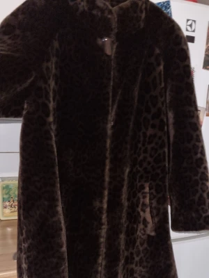 Leopardmönstrad fuskpälsjacka - Säljer en mörkbrun päls ( fusk) med leopardmönster. Tillverkad av C.D.V ( Comme Du Vrai) Paris  som specialiserat sig på just fuskpäls och är kända för sin höga kvalitet. Den har en lätt utställd passform, klockad  och knäpps med hyskknappar samt en stor knapp/knopp strax under kragen. Skön, varm,  stilig och elegant!                   Ärmlängd ( axel till hand) 60cm Baksida längd ( rygg till slut,krage ej inräknad) 85cm  Vidd byst 60cm ( framsida)  Kan maskintvättas i 30°