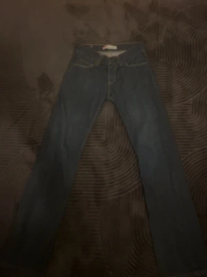 Levi's 506 raka blå jeans - Mörkblå raka jeans från Levi's modell 506 Standard. Klassisk femficksdesign med kontrastsömmar och bälteshällor. Tillverkade i slitstark denim som ger en tidlös look. Perfekta för dig som gillar enkel och clean stil.
