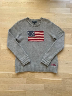 Grå stickad tröja Polo Ralph Lauren - Snygg grå stickad tröja från Polo Ralph Lauren med amerikansk flagga på bröstet och RL-broderi i rött vid nederkanten. Tröjan är Xl i ungdom och passar som en vanlig S-M. Ifall ni har frågor eller vill ha fler bilder är det att bara höra av sig // Mvh Partille closet 
