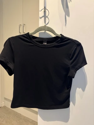 Svart croppad skims t-shirt - En enkel och stilren svart croppad t-shirt med rund hals och korta ärmar. Perfekt att matcha med höga jeans eller kjol för en clean look. Tillverkad i mjuk bomull för skön känsla hela dagen.