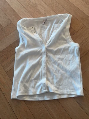 Vit ribbad linnetopp med knappar - Snygg vit ribbad linnetopp med knappar framtill. Toppen är ärmlös och har en enkel, clean look som passar till det mesta. Aldrig använt 