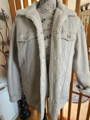Beige fodrad jeansjacka från H&M - Snygg beige jeansjacka från H&M med mjukt teddyfoder och krage. Klassisk modell med två bröstfickor med lock och knappar samt två sidofickor. Perfekt för dig som vill ha en stilren och varm jacka i jeansmaterial.
