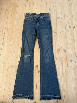 Blå bootcut jeans från Ginatricot - Säljer ett par blå bootcut jeans från  Gina i storlek 34.  Har klippt ut byxorna så att de blir längre, se bild 5. Är medelhög i midjan.  Annars bra skick. 