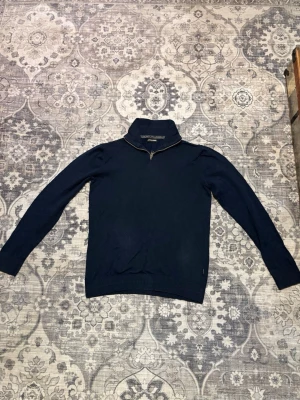 Mörkblå halvzip-tröja från Jack & Jones - Snygg mörkblå tröja från Jack & Jones med halvzip och hög krage. Tillverkad i mjukt material som känns skönt mot huden. Tröjan har långa ärmar och ribbade muddar vid ärmslut och nederkant. Perfekt för lager-på-lager och stilrena outfits. (Storlek S men passar mig som är 160 cm