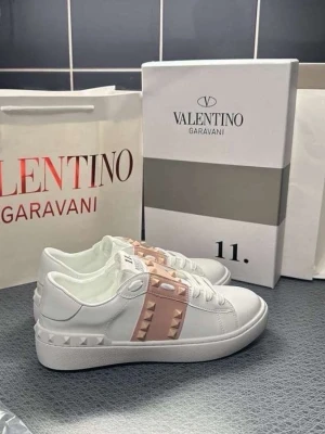 Valentino Garavani vita sneakers rosa  - Säljer ett par vita sneakers från Valentino Garavani med ljusrosa band och ikoniska nitar på sidan och hälen. Storlek 37-39