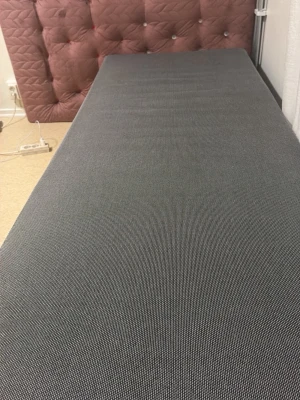  Sänk  - Säljer en stilren enkelsäng med grå madrass och en quiltad rosa sänggavel med dekorativa knappar. Sängen har en modern look och passar perfekt i sovrummet eller gästrummet. Enkel design som funkar till många olika inredningsstilar.