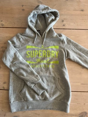 Grå hoodie från Superdry - Säljer en grå vintage Superdry hoodie i storlek S. Tröjan är i mycket gott skick och har en normal passform. Perfekt nu till våren! Skriv om vid funderingar!🙌🙌☀️☀️