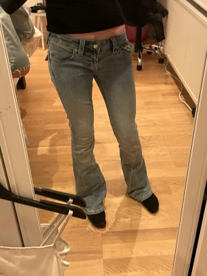 True Religion Joey Low Rise Flare Jeans - Säljer ett par ljusblå True Religion Joey jeans med låg midja och utsvängda ben. Klassisk femficksmodell i denim med snygga slitningar och detaljerade sömmar. Perfekta för dig som gillar retrovibbar och en avslappnad men trendig look.