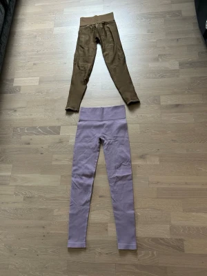 Ljuslila ribbade leggings med hög midja och bruna leggings - Säljer ett par ljuslila leggings med ribbad struktur och hög midja ifrån Lindex och ett par leggings i brun ifrån HM. De är stretchiga och har en tight passform som framhäver benen. Perfekta för en avslappnad och trendig look. Materialet känns mjukt och följsamt mot huden.